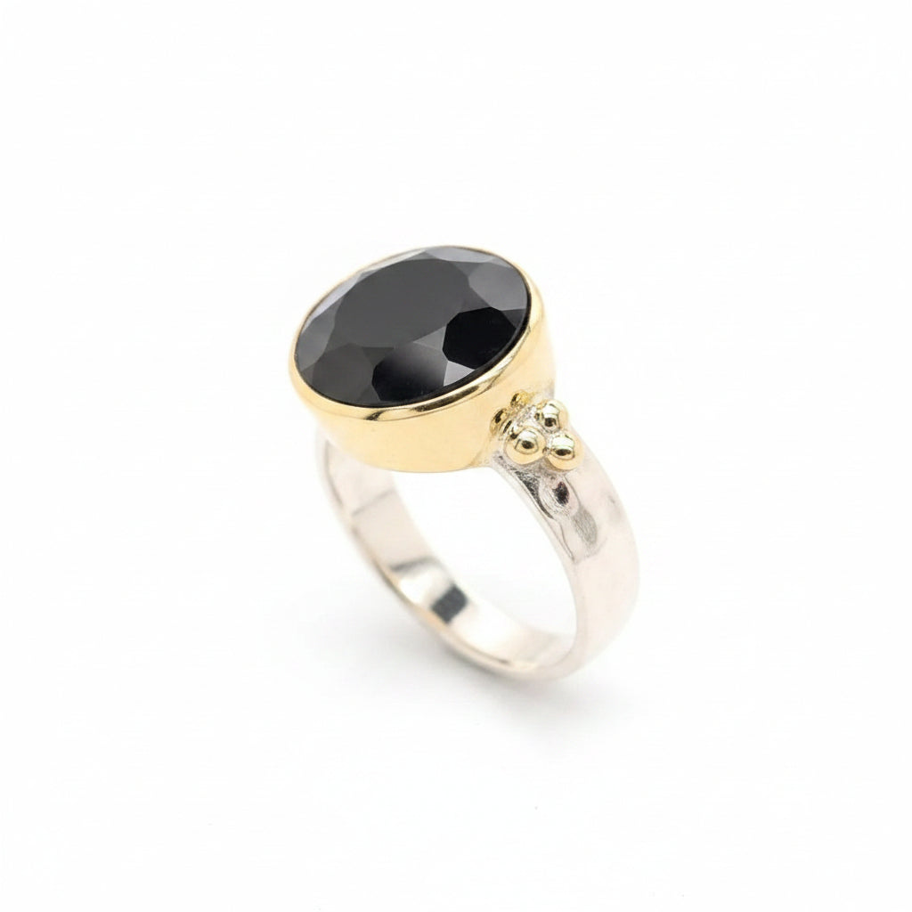 A striking black onyx cut gem rests in a warm gold circle setting on a sleek flat band sterling silver ring