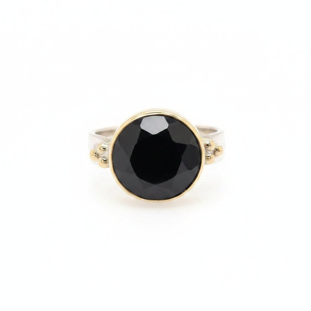 A striking black onyx cut gem rests in a warm gold circle setting on a sleek flat band sterling silver ring
