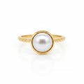 A delicate pearl embraced by a pond of gold resting on a fine patterned round band ring
