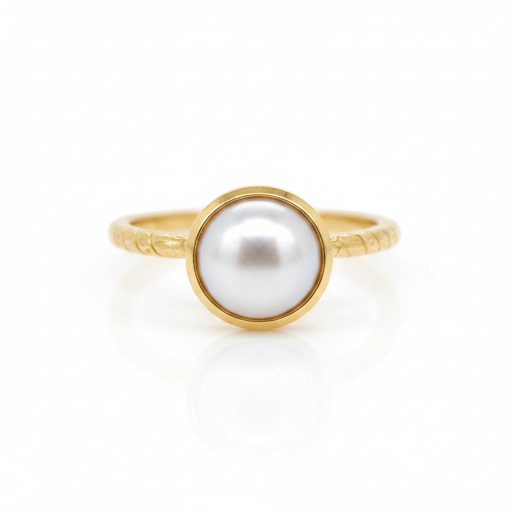 A delicate pearl embraced by a pond of gold resting on a fine patterned round band ring