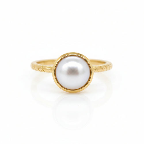 A delicate pearl embraced by a pond of gold resting on a fine patterned round band ring
